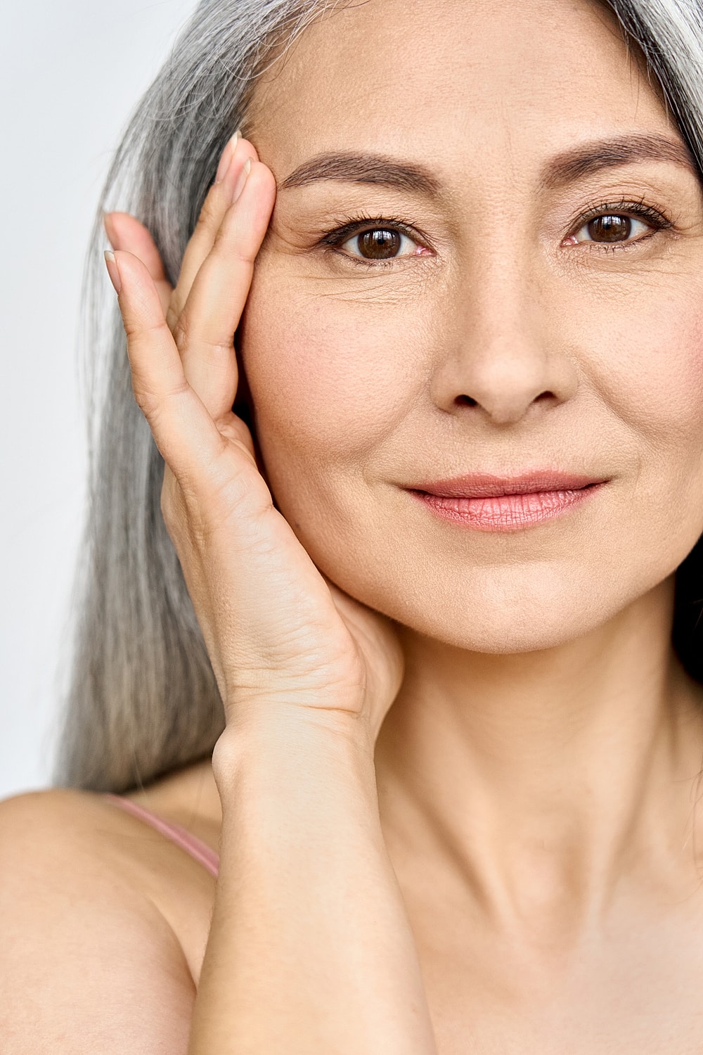 Woman with gray hair touching her face.