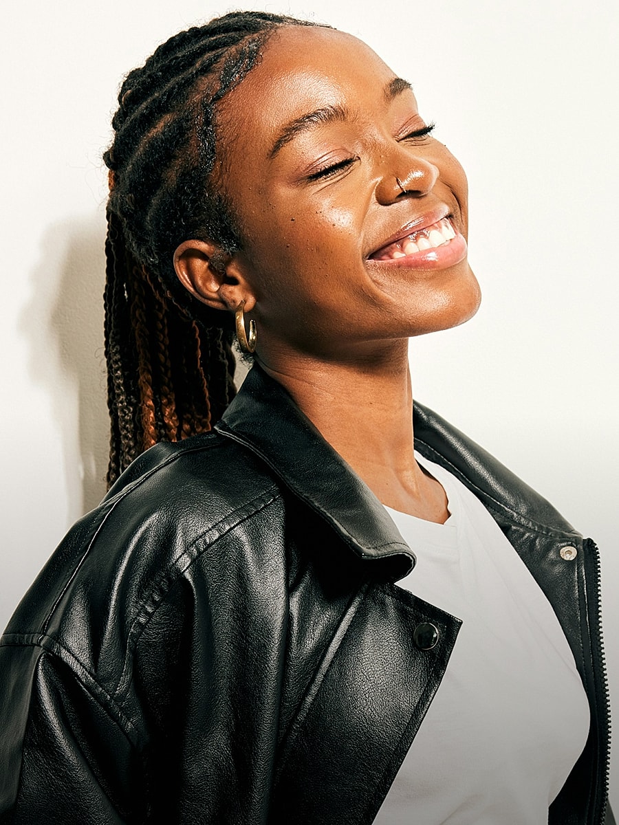 Smiling person with braided hair in leather jacket.